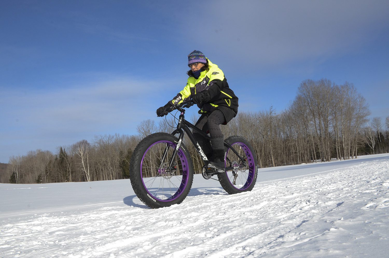 A fat-bike rider in a bright yellow jacket riding across packed snow under a blue winter sky in Iron County