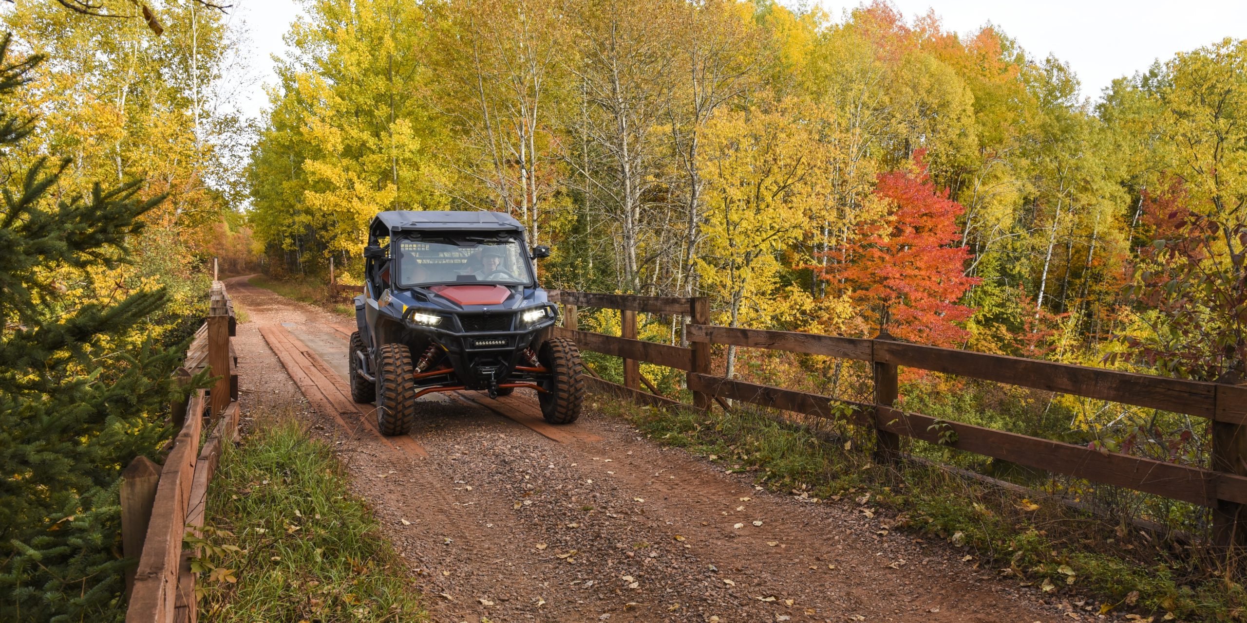A side-by-side ATV riding along a tree-lined trail in Iron County, Michigan, surrounded by vibrant yellow and red and orange autumn leaves on a fall day.