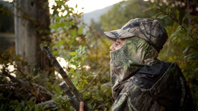 Young hunter in camo near water in the forest with rifle preparing for the hunt