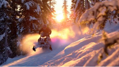 a snowmobile full throttle through the deep snow deep woods sunsetting