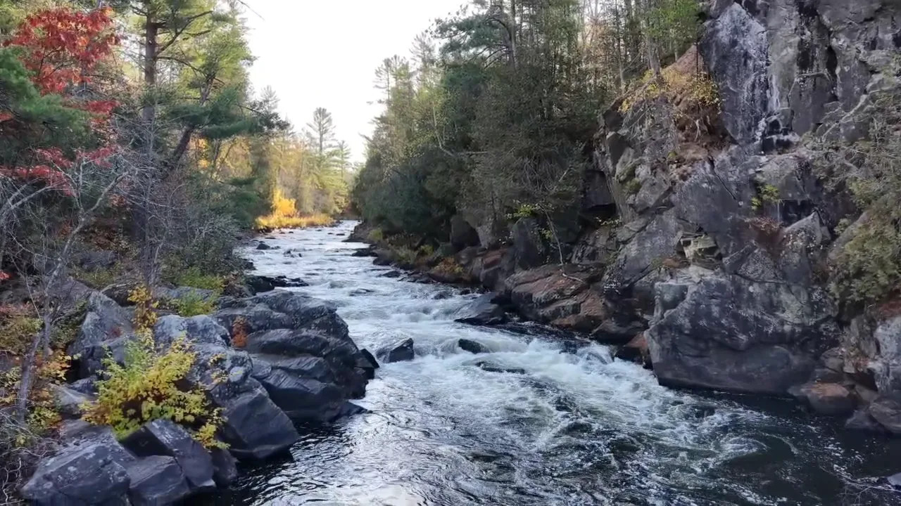 Whitewater rushing past dark rock cliffs and fall color at Horserace Rapids on the Paint River