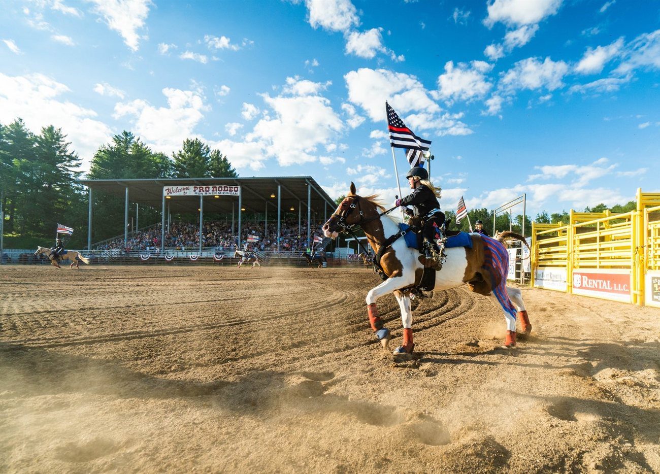 A rider carrying the American flag at a gallop past the grandstand at the U.P. Championship Rodeo
